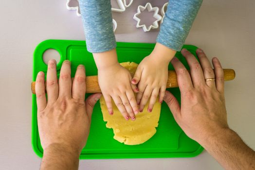 Children and dad hands rolled shortcrust dough with a rolling pin on the table