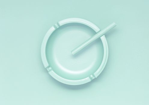 Creative concept photo of a painted ashtray with a cigarette on mint background.