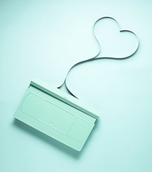 Creative love concept photo of painted VHS cassette with tape in the shape of heart on mint background.