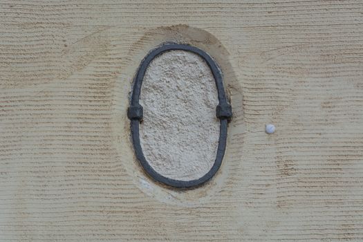 Rusty antique wall anchor in an old yellow painted and plastered stone wall.