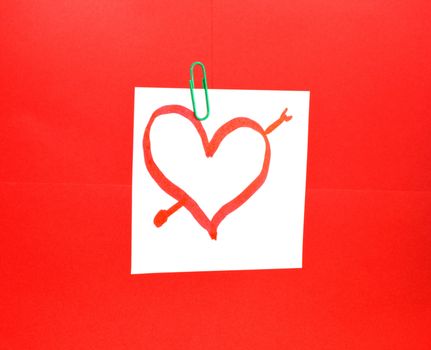Heart drawn on a post it in front of a red background