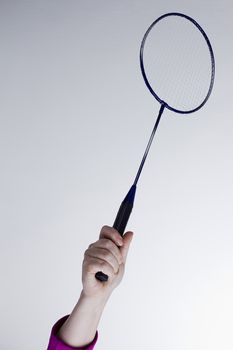 Female hand with a badminton racket on a gray background