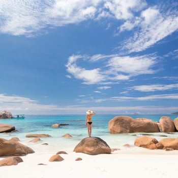 Woman wearing black bikini and beach hat, enjoying amazing view on Anse Lazio beach on Praslin Island, Seychelles. Summer vacations on picture perfect tropical beach concept.