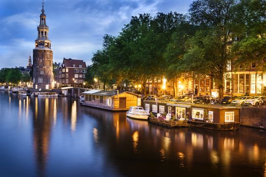 Beautiful night in Amsterdam. Night illumination of buildings and boats near the water in the canal.