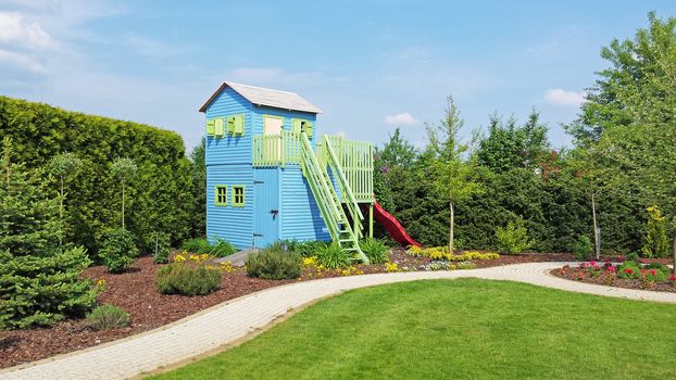 Wooden play house for kids in corner of the garden. Summer time, good sunny weather.