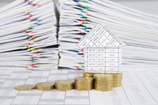 Close up house and step pile of gold coins on finance account have blur pile overload paperwork of report and receipt with colorful paperclip as background.