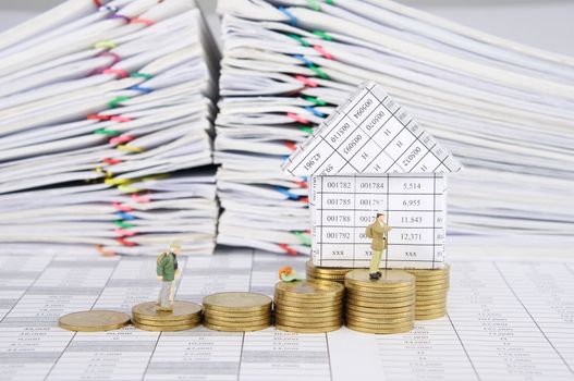 Close up traveler with step pile of gold coins and house on finance account have blur pile overload paperwork of report and receipt with colorful paperclip as background.