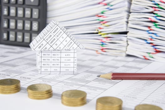 House and pencil on finance account have blur pile of gold coins with calculator place vertical and pile overload paperwork of report and receipt with colorful paperclip as foreground and background.