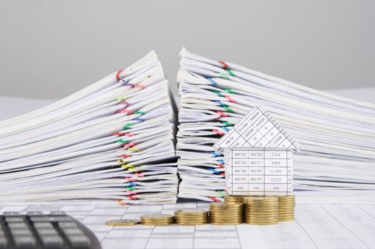 House and step pile of gold coins on finance account have blur calculator and pile overload paperwork of report and receipt with colorful paperclip as foreground and background.