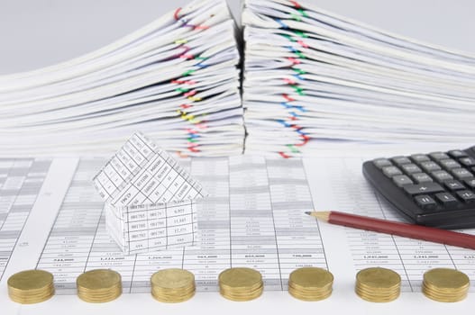 House on finance account have blur pile of gold coins with pencil and calculator with pile overload paperwork of report and receipt with colorful paperclip as foreground and background.