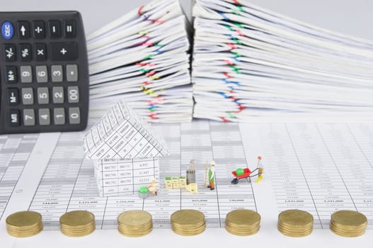 House with farmer on finance account have blur pile of gold coins place as fence with calculator and pile overload paperwork of report and receipt with colorful paperclip as foreground and background.