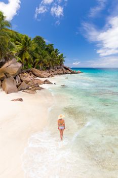 Woman wearing retro striped bikini and beach hat, enjoying amazing view on Anse Patates beach on La Digue Island, Seychelles. Summer vacations on picture perfect tropical beach concept.