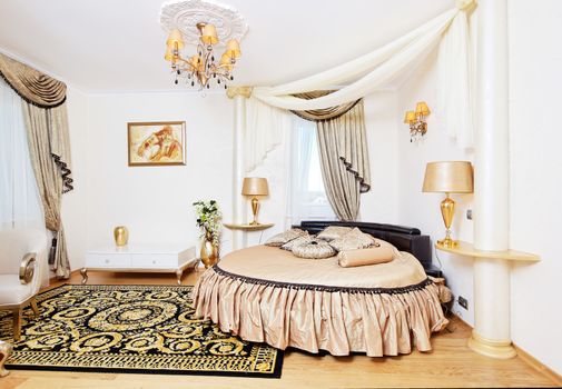 Golden classical bedroom interior with round bed and small table. Bedroom interior design. 