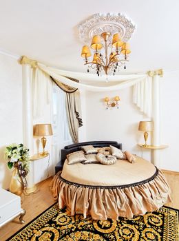 Golden classical bedroom interior with round bed and ornate ceiling