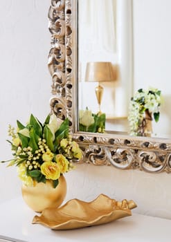 Golden vintage vase with flowers near beautiful antique mirror
