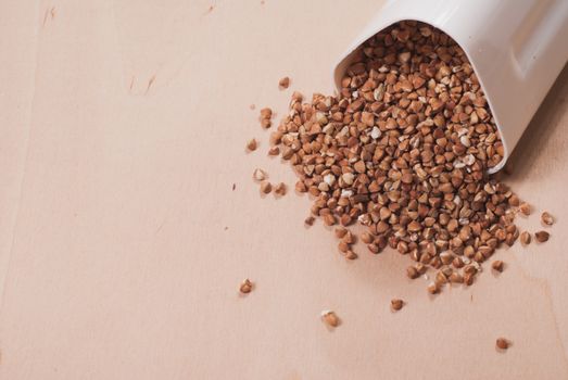 Buckwheat is scattered from the white container, wooden table, healthy food concept