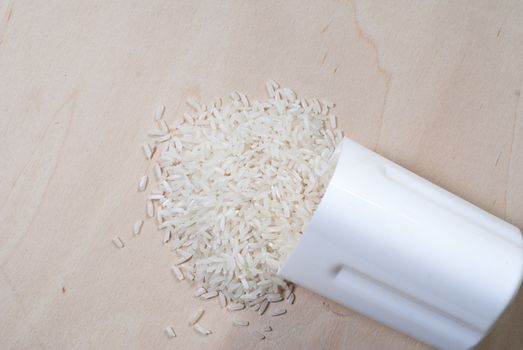 Rice scattered on the wooden surface, rice cereal in the white container, the concept of healthy eating