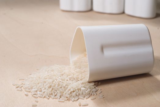 Rice scattered on the wooden surface, rice cereal in the white container, the concept of healthy eating