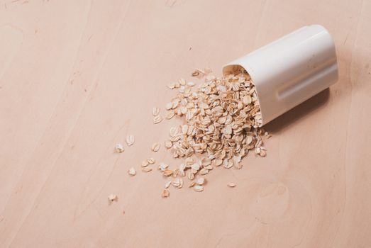 Oats scattered on the wooden surface, oatmeal in a white container, the concept of healthy eating