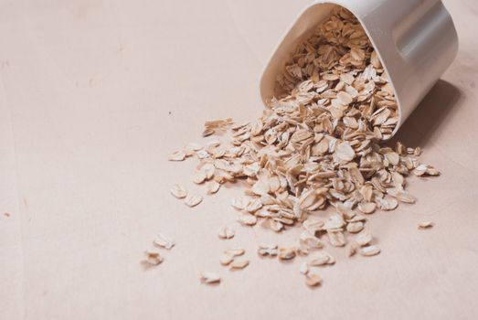 Oats scattered on the wooden surface, oatmeal in a white container, the concept of healthy eating