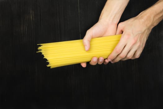 Top view bunch of  raw spaghetti in male hands on black wood vintage table