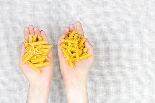 Female hands holding heap of raw fussilli and penne noodles on white canvas background