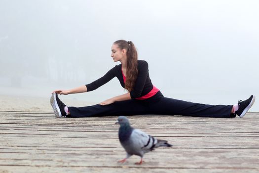 Young pretty slim fitness sporty woman does stretching exercises during training workout outdoor