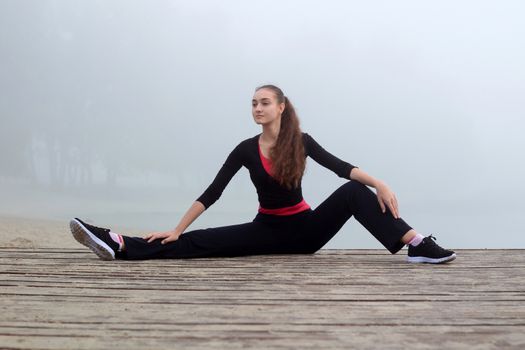 Young pretty slim fitness sporty woman does stretching exercises during training workout outdoor