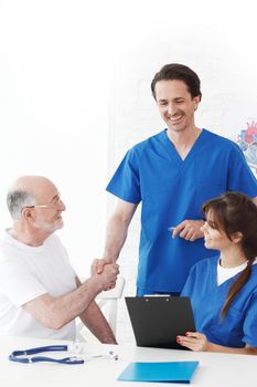 Happy senior patient and doctors in hospital shaking hands