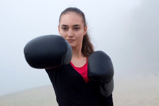 Young pretty slim fitness sporty woman does boxing exercises during training workout outdoor