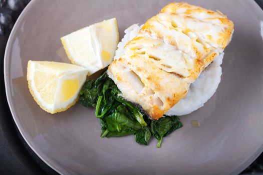Fried cod fillets, spinach and lemon on the plate