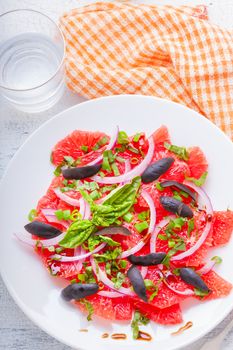 Grapefruit salad with olives, red onion, basil on the table