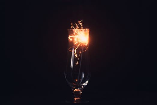 Sparkler on a black background, sparks fly in different directions, elegant glass, Christmas atmosphere