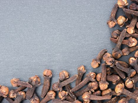 Cloves spice on gray slate background with copy space. Isolated one edge. Top view or flat lay.