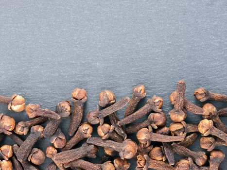 Cloves spice on gray slate background with copy space. Isolated one edge. Top view or flat lay.