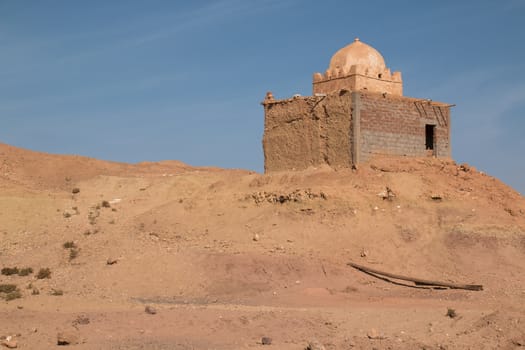 Old and not finished construction of a mosque on hill beside the road to the city Ait Ben Haddou. Dome without a tower. Bright blue sky. Orange sandy soil.