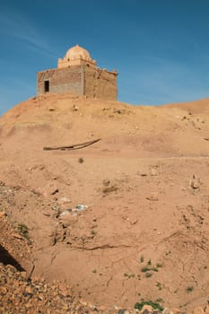 Old and not finished construction of a mosque on hill beside the road to the city Ait Ben Haddou. Dome without a tower. Bright blue sky. Orange sandy soil.