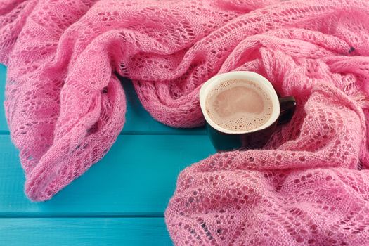 Cozy winter home background, cup of hot cocoa with marshmallow, old vintage books and warm knitted sweater on white painted wooden board background.
