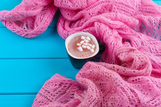 Cozy winter home background, cup of hot cocoa with marshmallow, old vintage books and warm knitted sweater on white painted wooden board background.
