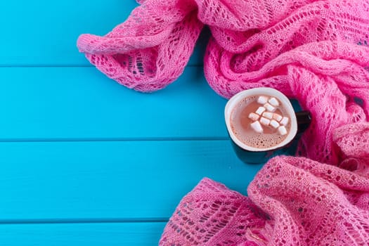 Cozy winter home background, cup of hot cocoa with marshmallow, old vintage books and warm knitted sweater on white painted wooden board background.