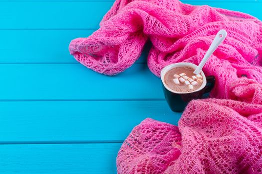 Cozy winter home background, cup of hot cocoa with marshmallow, old vintage books and warm knitted sweater on white painted wooden board background.