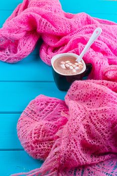 Cozy winter home background, cup of hot cocoa with marshmallow, old vintage books and warm knitted sweater on white painted wooden board background.