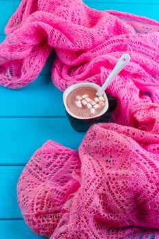 Cozy winter home background, cup of hot cocoa with marshmallow, old vintage books and warm knitted sweater on white painted wooden board background.