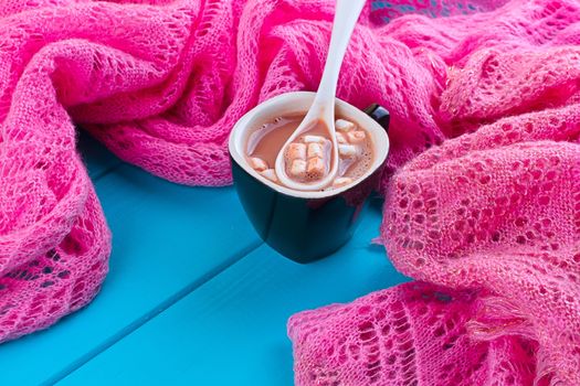 Cozy winter home background, cup of hot cocoa with marshmallow, old vintage books and warm knitted sweater on white painted wooden board background.