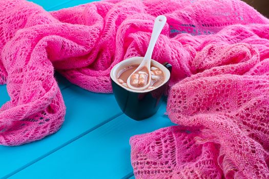 Cozy winter home background, cup of hot cocoa with marshmallow, old vintage books and warm knitted sweater on white painted wooden board background.