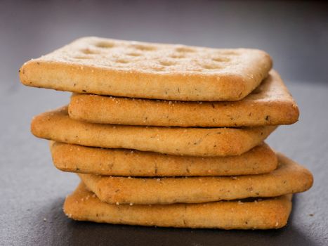 stack of square crackers on slate gray background. Dry salt cracker cookies with fiber and dry spices