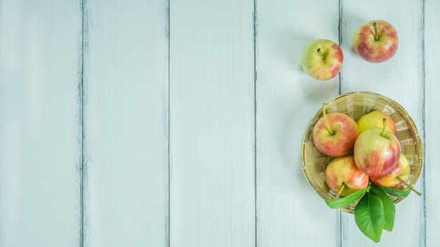 Top view red and yellow apple with leaves and  bamboo basket on  white wooden background with free space for text