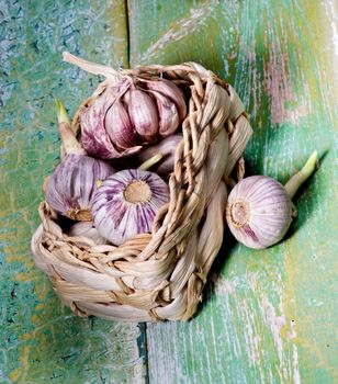Arrangement of Fresh Pink Garlic with Green Stems in Wicker Basket closeup on Cracked Wooden background