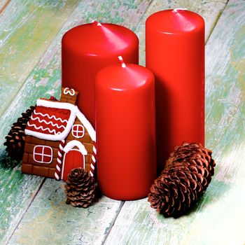 Christmas Decoration Concept with Red Candles, Fir Cones and Gingerbread House closeup on Cracked Wooden background
