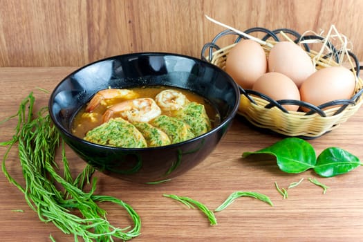 Hot and sour soup curry with shrimps and acacia pennata omelette. In black dish on wood table.